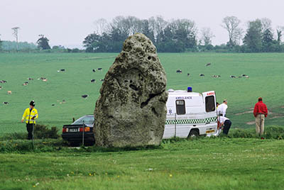 ENG: South West Region, Wiltshire, Central Chalklands, Salisbury Plain, Stonehenge, A view past the Heel Stone to an ambulance a few feet behind it, on the A344 highway, where an auto accident had occured. [Ask for #197.080.]