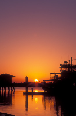 Sun rising behind docks; view towards St. Augustine Harbor; excursion boat (rt) in the style of a riverboat. Location: FL, St. Johns County, St. Augustine, Municipal Yacht Pier. [ref. to #231.007]