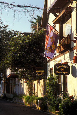 View down Charlotte Street; Spanish Colonial house decorated with flags; shop signs for "Moultrie Creek Studios Gallery" & "Candida's Boutique". Location: FL, St. Johns County, St. Augustine, The Old City. [ref. to #231.025]