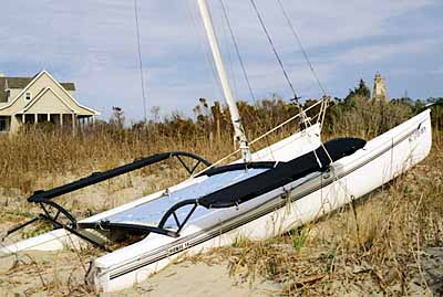 Catamaran beached on dunes; Bald Head Lighthouse (Old Baldy) in bkgd, rt. Location: NC, Brunswick County, Cape Fear Area, Bald Head Island, West Beach. [ref. to #233.055]