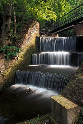 Water cascades over a mill pond's brick weir, in these ruins from an 18th C. copper rolling plant, now in a forest. Location: WAL, Flintshire County, Clwydian Hills, Holywell, Greenfields Valley Heritage Park. [ref. to #246.071]