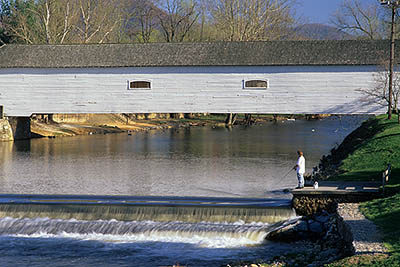 TN: The Northern Mountains Region, Carter County, Watauga River Area, Elizabethton, Doe River Covered Bridge (1887), Afternoon view in early spring; weir in frgd; man fishing from weir. NR [Ask for #252.028.]