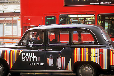 A classic London black taxi, covered with colorful advertising, waits outside a rail station. NR. Location: ENG, Greater London , City of Westminster, Victoria Station, Station Exterior. [ref. to #256.104]