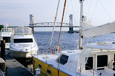 NC: New Hanover County, Cape Fear River Area, Wilmington, Riverfront, River Walk. View of Cape Fear Bridge over yachts moored by walk [Ask for #263.065.]