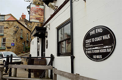 ENG: Yorkshire & Humberside Region, North Yorkshire, North Yorkshire Coast, Sea Cliffs, Robin Hood's Bay, Stone cottages, perched on cliff terrace, front on stone-paved foot-only lane; the harbor-side Bay Hotel marks the start of the Coast-To-Coast walk, an ldp [Ask for #270.081.]